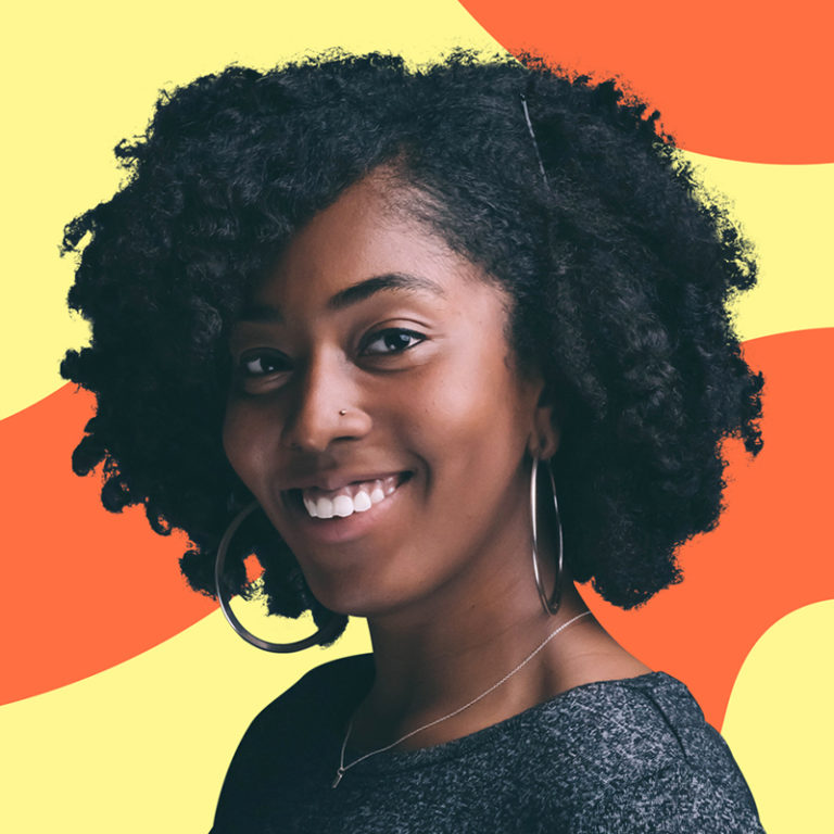 A joyful woman with curly hair and large hoop earrings smiling against a vibrant orange and red background.