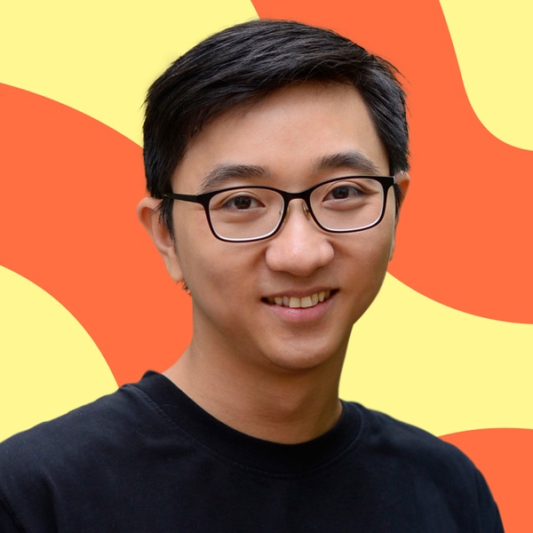 A young asian man with glasses smiling against a colorful red and yellow abstract background. he wears a black t-shirt and looks directly at the camera.