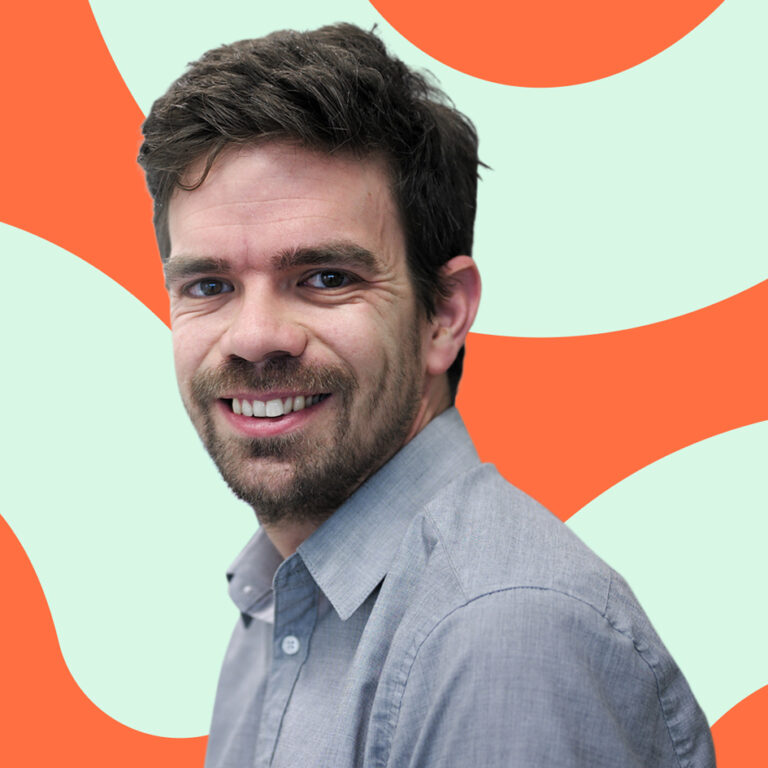 A smiling man with dark hair and a beard, wearing a grey shirt, set against a playful orange and teal abstract background.