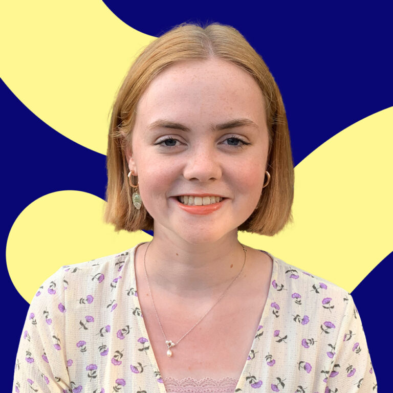 A smiling young woman with short blonde hair wearing a light purple top with floral patterns against a graphic blue and yellow background.