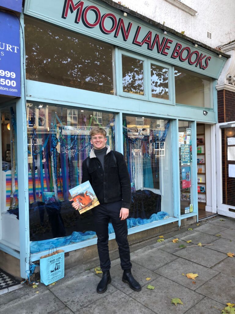Macken Murphy holding a copy of Animal Sidekicks in front of the Moon Lane bookshop.