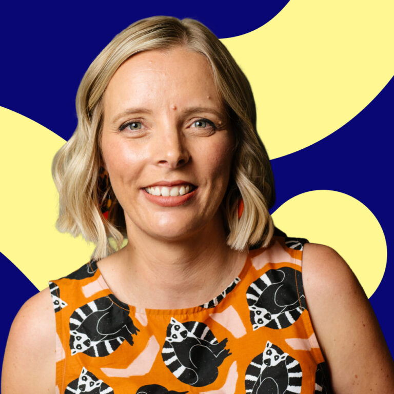 A smiling woman with blonde hair wearing a colorful orange dress with black and white fish patterns, against a blue background with yellow abstract shapes.