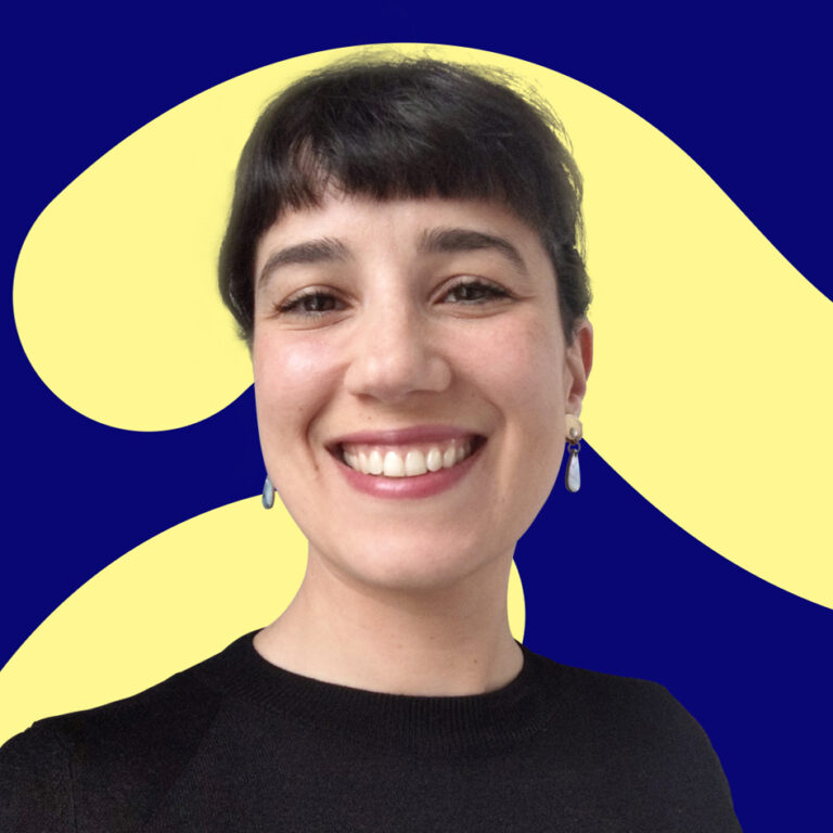 A smiling woman with short dark hair and blue earrings, against a blue background with abstract yellow shapes. she wears a black top.