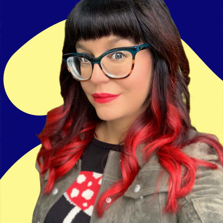 A woman with black and red hair, wearing glasses and red lipstick, smiles against a blue and yellow abstract background. she has a stylish, modern look.