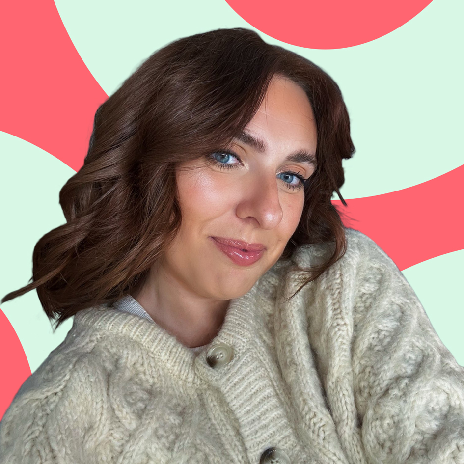 Woman with wavy brown hair wearing a sweater, smiling in front of a colorful abstract background.