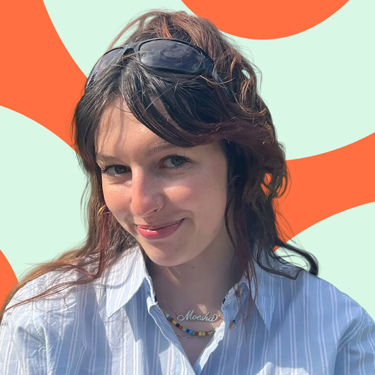 Smiling woman with sunglasses on her head, striped shirt, and necklace, in front of an orange patterned background.